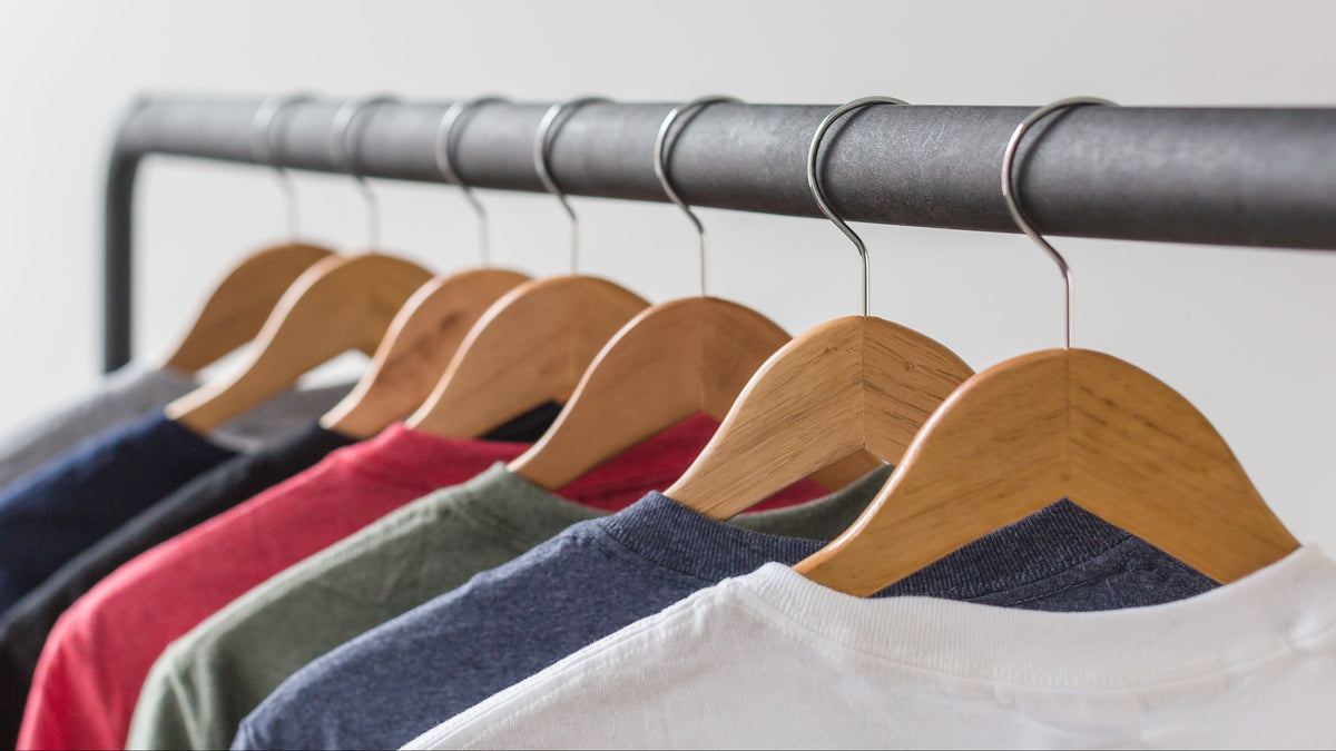 Row of shirts on wooden hangers against a plain background